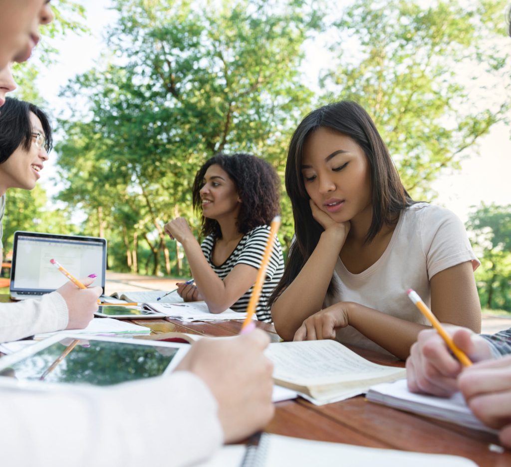 Picture of multiethnic group of young students sitting and studying outdoors while talking. Looking aside.